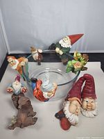 Lot overview showing multiple gnome figures attached to rim of clear glass bowl, additional figurines surrounding