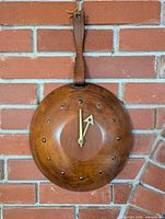 Front view of maple wall clock showing brass studs and leather strap