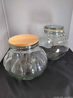 Two clear glass canisters, one with wood lid, one with clamp lid