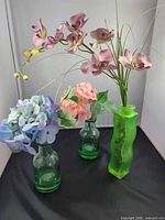 Overview of three green frosted glass vases with artificial flowers