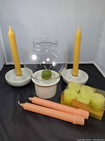 Full lot showing candlestick holders with yellow tapers, glass hurricane lamp with base and votive, peach tapers and boxed Claire Burke votives