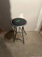 Full view of gray metal folding stool with round black seat