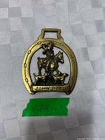 Front view of the brass ornament showing John Peel design within horseshoe frame