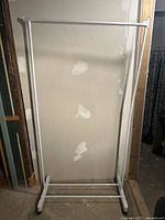 Full view of white garment rack showing hanging bar, lower rails and casters