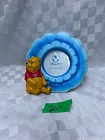 Front view of blue flower-shaped Disney Store frame with seated Winnie the Pooh figure, green tape marked 200 for lot context
