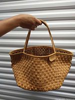 Full view of woven leather Bree basket bag held by hand
