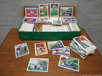 Long green storage box filled with trading cards, several Looney Tunes and NFL cards spread on table