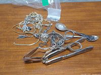 Lot overview showing tangled jewelry, spoon, and two scissor tongs