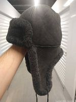 Left side view of black shearling trapper hat showing ear flap and suede exterior