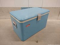 Front view of baby blue Coleman Snow-Lite metal cooler showing logo and latch