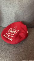 Full view of red beret on couch showing embroidered maple leaf logo