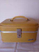 Front view of closed Neevel Lite-Pac mustard train case showing handle, latch and emblem