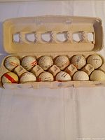 Open egg carton showing all 12 Spalding red-striped golf balls