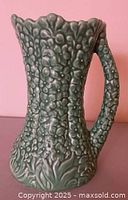 Front view of embossed green vase with handle and scalloped rim