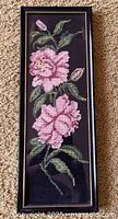 Full view of framed floral needlepoint showing pink flowers on black background.