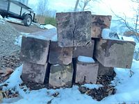 Stacked ends of square timbers showing 8×8 in cross-section, weathering and cracks
