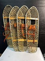 two complete pairs of wooden snowshoes with rawhide webbing and leather bindings