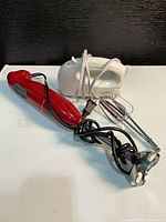 White hand mixer, red immersion blender, chrome beaters on tabletop