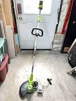 Full view of assembled Greenworks string trimmer standing upright with battery inserted; charger on floor