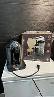Front view of Nespresso Vertuo machine next to box