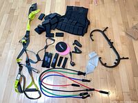 All items laid out on floor: weighted vest, weights, suspension trainer, resistance bands set, sliders, straps, massage cane