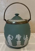 Front view of sage green Wedgwood biscuit barrel jar showing classical relief and silver-plated rim with handle raised