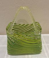 Front view of striped green-yellow art glass purse vase with clear handles