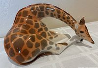 Left side view of seated porcelain giraffe showing glaze and spot pattern