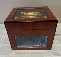 Three-quarter view of closed music box showing wood case and glass front panel