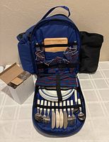 Open backpack showing plates, cutlery, napkins, cutting board, glasses and tools