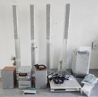 Full lot showing four column speakers, micro hi-fi receiver with two bookshelf speakers, subwoofer, amplifier, cables and remotes
