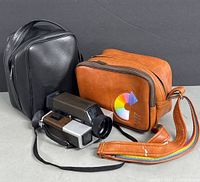 Group shot of Kodak camera, black vinyl bag, tan leatherette case with rainbow strap