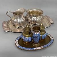 All seven pieces grouped together, showing cloisonné set in front and silverplate set behind