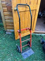 Full view of red metal hand dolly standing against shed door