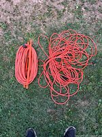 Two orange extension cords on grass, showing overall lot