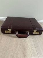 Closed burgundy hard briefcase lying flat, showing gold combination locks and handle