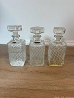 Front view of three matching clear pressed glass decanters with stoppers