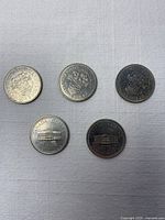 Five commemorative Canadian dollar coins arranged; three BC (top), two PEI (bottom)