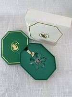 Ornament in open green box alongside outer white sleeve