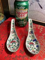 Front view of both floral porcelain spoons with size reference can