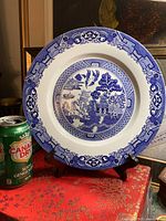 Front of Blue Willow plate on stand next to can for scale