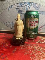 Full view of resin scholar figurine on stand beside soda can for scale