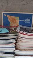 Two stacks of assorted magazines and Atlas of British Columbia behind