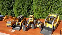 All five construction vehicles and two loose buckets lined up on table