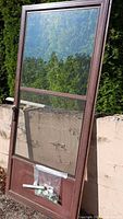 Front view of brown aluminum screen door with glass upper section, screen lower section, hardware bag visible