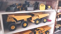 Three small front-end loaders, detached bucket, small bulldozer on top shelf, two large steel dump trucks and red car on middle shelf