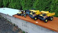 five Tonka construction vehicles lined up on wooden surface outdoors