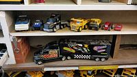 Shelf with six small toy vehicles and one large black semi with trailer