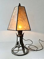 Front view of metal table lamp lit, showing mica shade and base detail