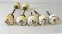Front view of five of the porcelain floral door knobs with spindles attached showing decoration and hardware